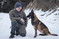 Éducateur accroupi dans la neige à côté d'un malinois assis
