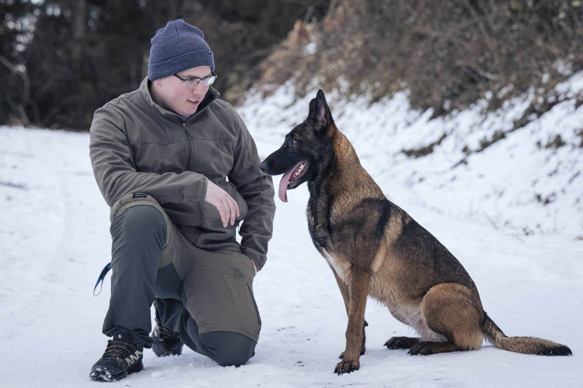 Sacha, éducateur canin, accroupi dans la neige face à un berger malinois