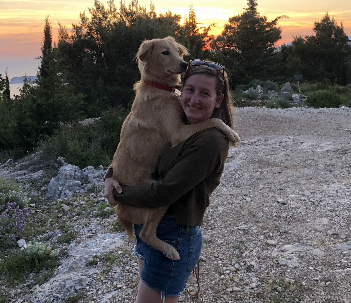 Victoria porte un golden retriever dans ses bras au coucher du soleil